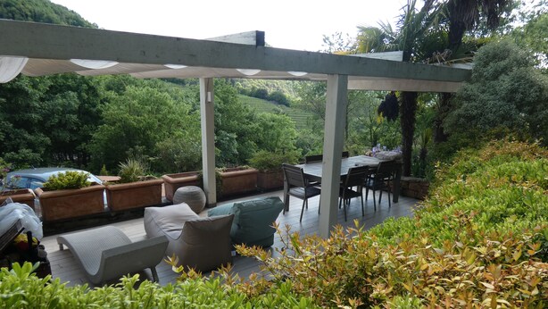Een terras buiten met een pergola, zitgedeelte en potplanten.