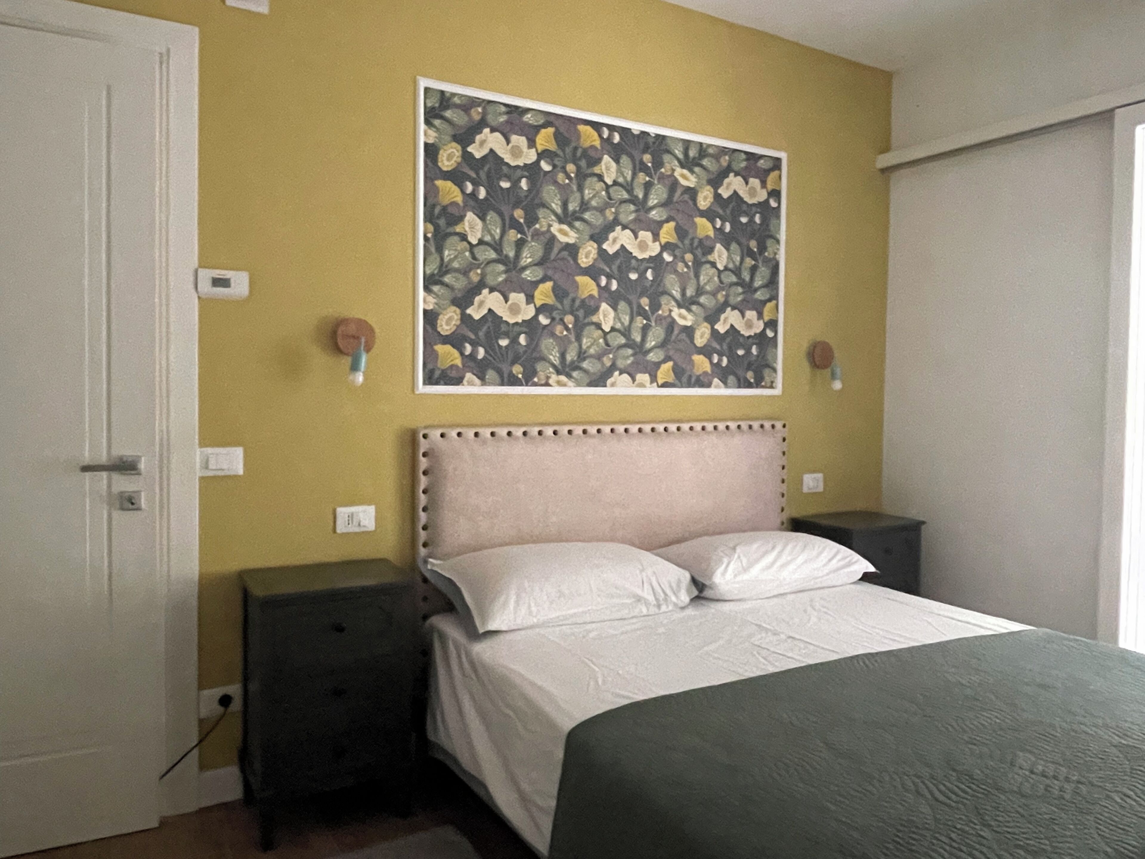 Ein Schlafzimmer mit einem Bett, Nachttischen, einem Wandbild und einer Tür.