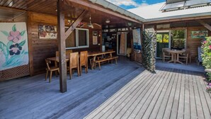 Una terraza exterior de madera con mesas y sillas de madera, un área de estar cubierta y una parrilla.