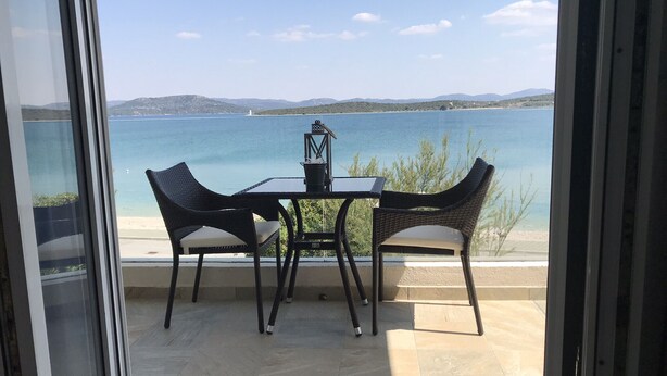 A balcony with a table and two chairs, overlooking a body of water and distant hills. - Villa Danica - Apartment (studio) 2 persons - direct at sea - 4 star (Betina)