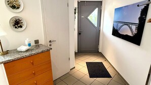 Ein Flur mit Küchenzeile, einer grauen Tür, einer schwarzen Matte und einem gerahmten Bild an der Wand.
