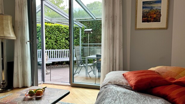 Ein Zimmer mit einem Bett, einem Tisch mit Obst, einer Bank draußen und einem Gemälde an der Wand.