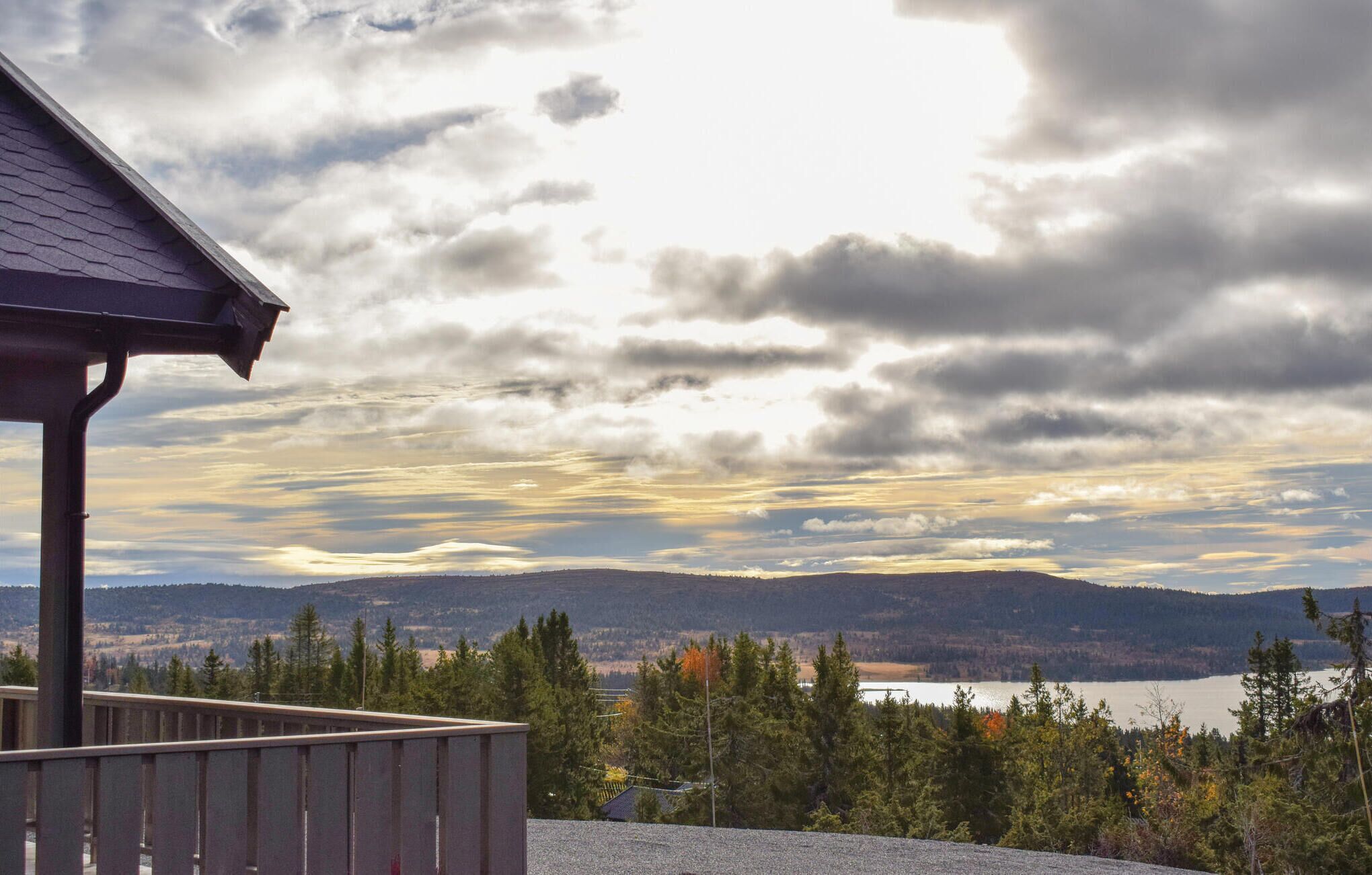 A wooden deck overlooking a lake with mountains in the distance and a cloudy sky.