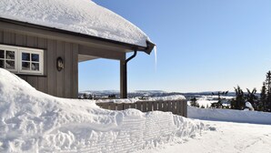 A snow-covered house with a clear view of a snowy landscape and distant mountains.