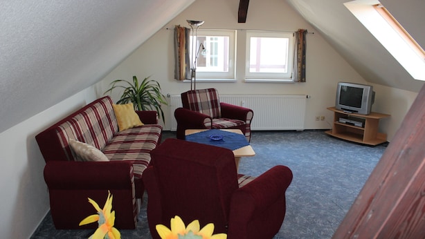 A cozy attic living room with a red sofa, a plaid armchair, a small table, and a television on a wooden stand. - Apartment 1 "Auerhahn" up to 4 persons + cot - dog allowed (Wernigerode)