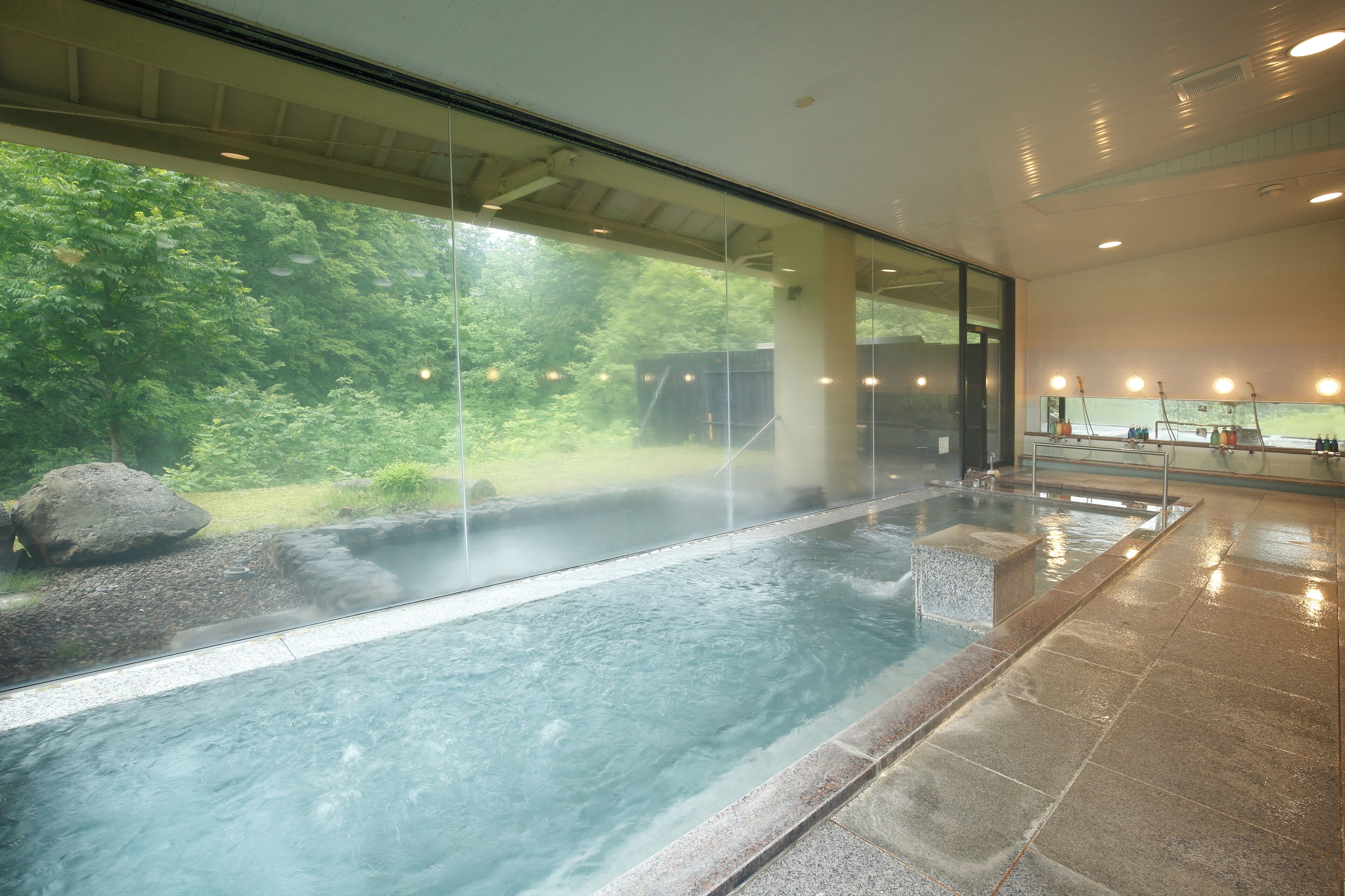 A spa area with a hot spring, glass walls, and a view of greenery.