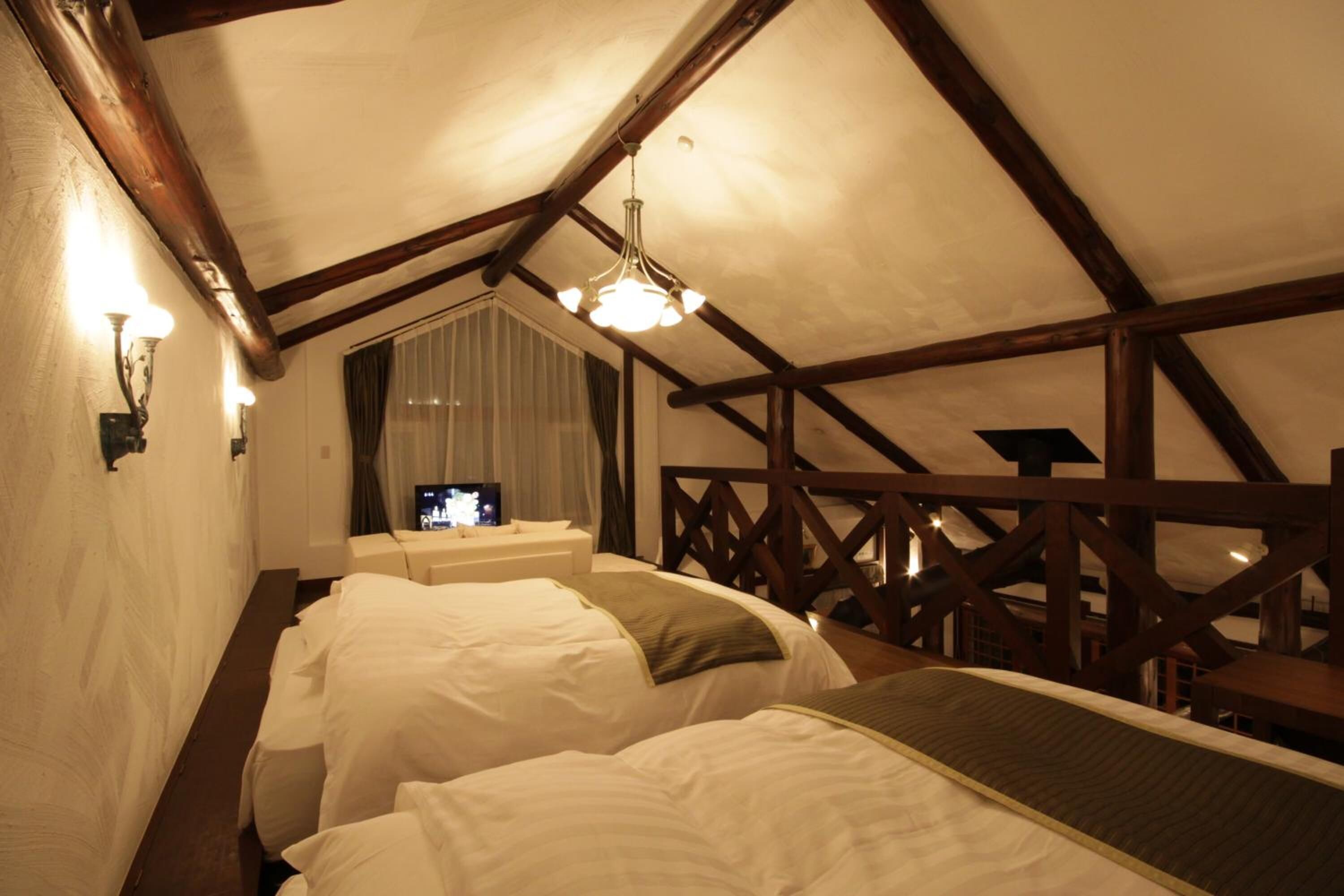 Een gezellig slaapkamer op zolder met twee bedden, houten balken, een televisie en een raam met gordijnen.