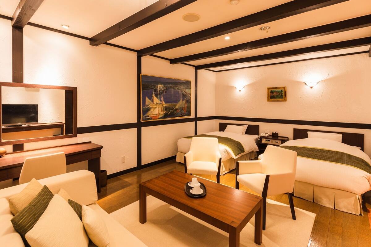 Ein Hotelzimmer mit Holzboden, einem Fernseher, einem Gemälde und zwei Betten mit weißer Bettwäsche.