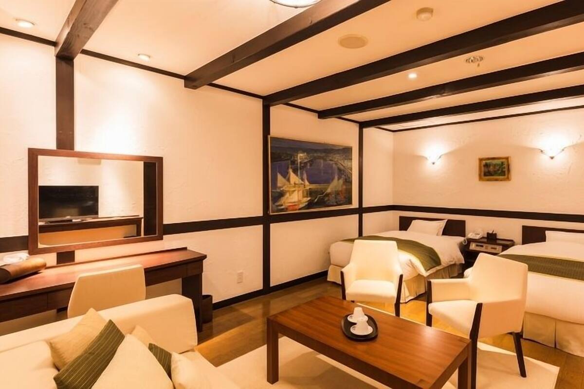 Ein Hotelzimmer mit einem Bett, zwei Stühlen, einem Schreibtisch, einem Fernseher und Bildern an den Wänden.
