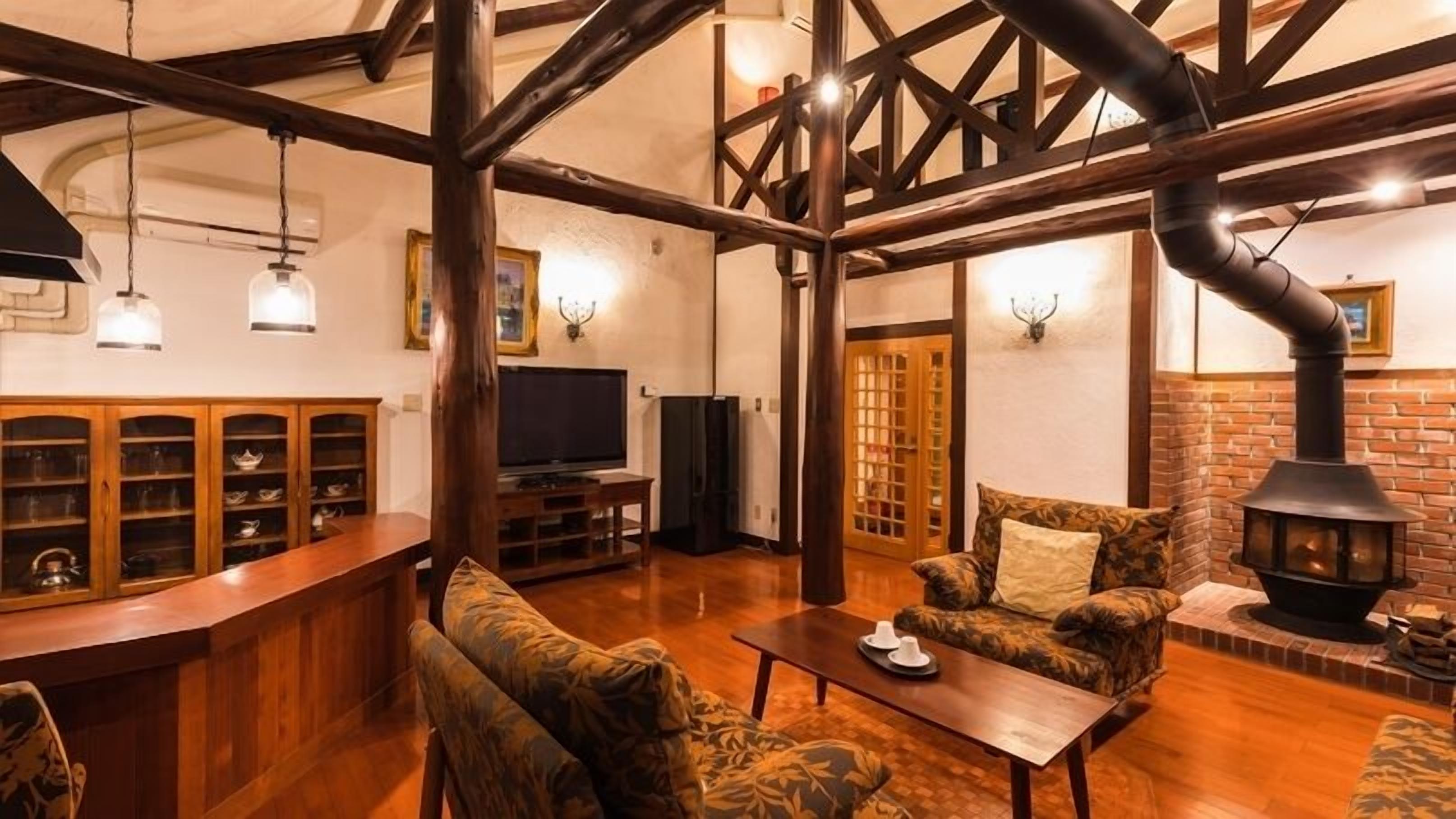 A cozy living room with a fireplace, wooden beams, a television, and a bar area.