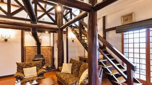 A cozy living room with a fireplace, wooden beams, a staircase, and patterned furniture. - Hotel Jogakura (Aomori)