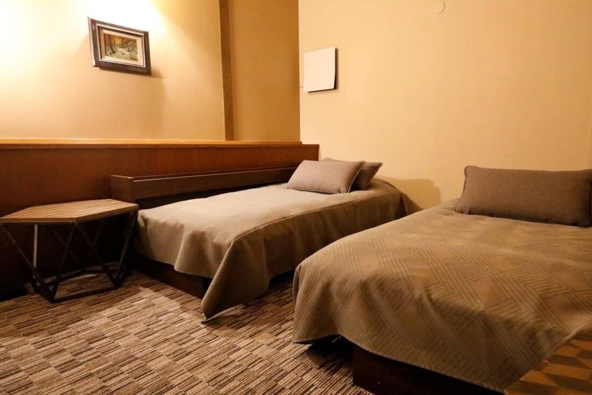 A hotel room with two single beds, a small table, and a wall-mounted picture.