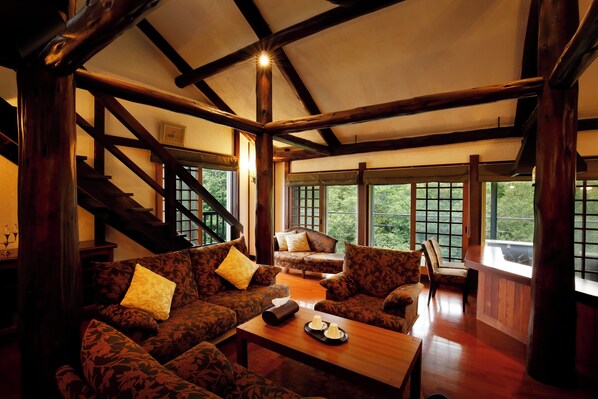 A spacious living area with a high ceiling, wooden beams, and large windows offering a view of the outdoors. - Hotel Jogakura (Aomori)