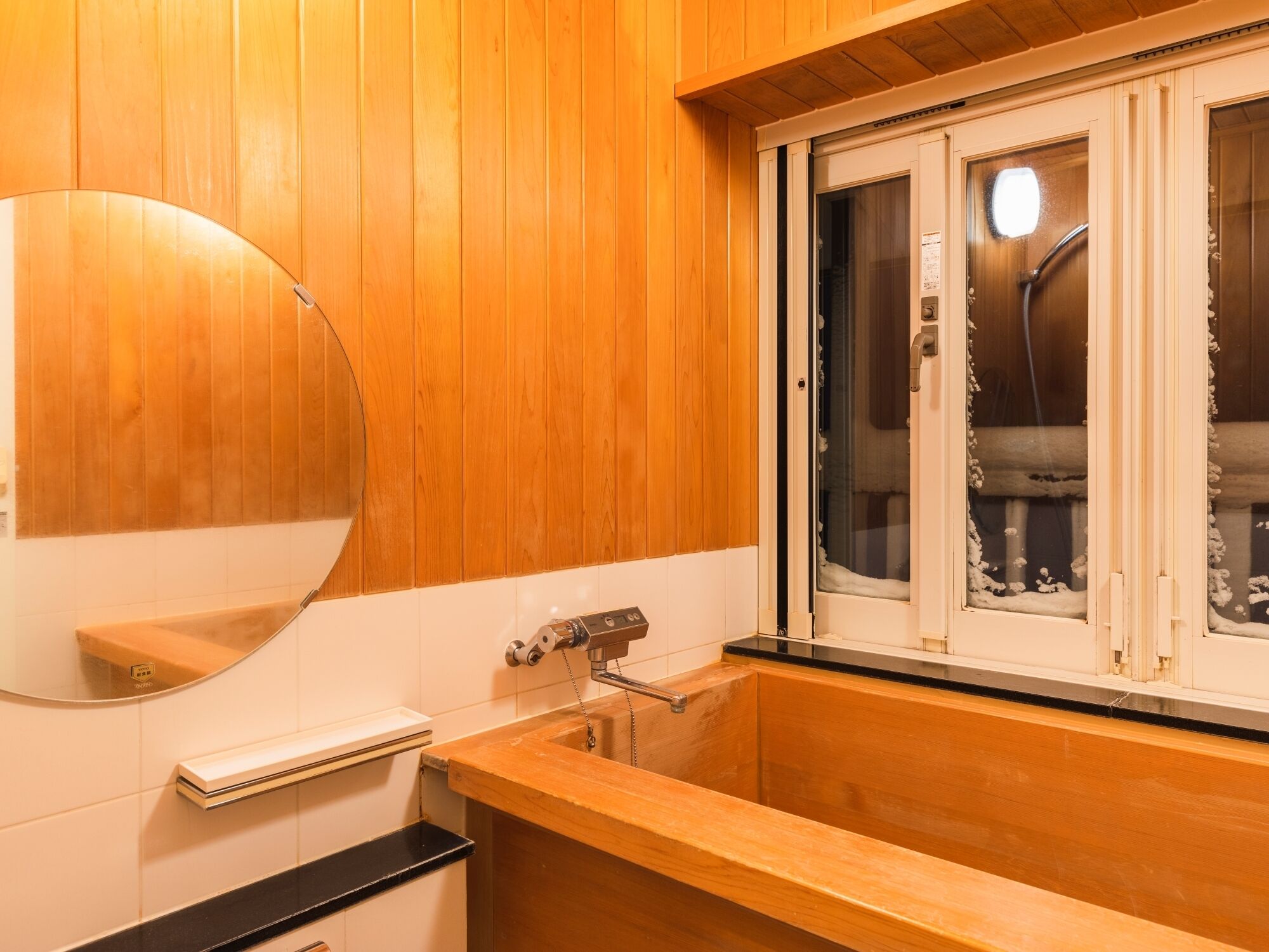 A wooden-paneled bathroom with a large mirror, a sink, and a window with frosted glass.