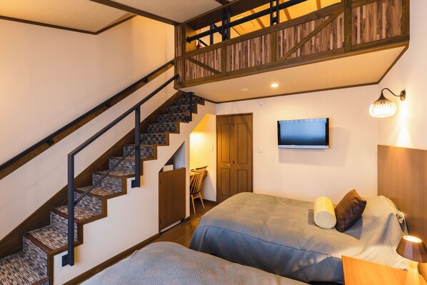 A bedroom with a wooden staircase, a bed with pillows, a TV on the wall, and a bedside lamp. - Hotel Jogakura (Aomori)