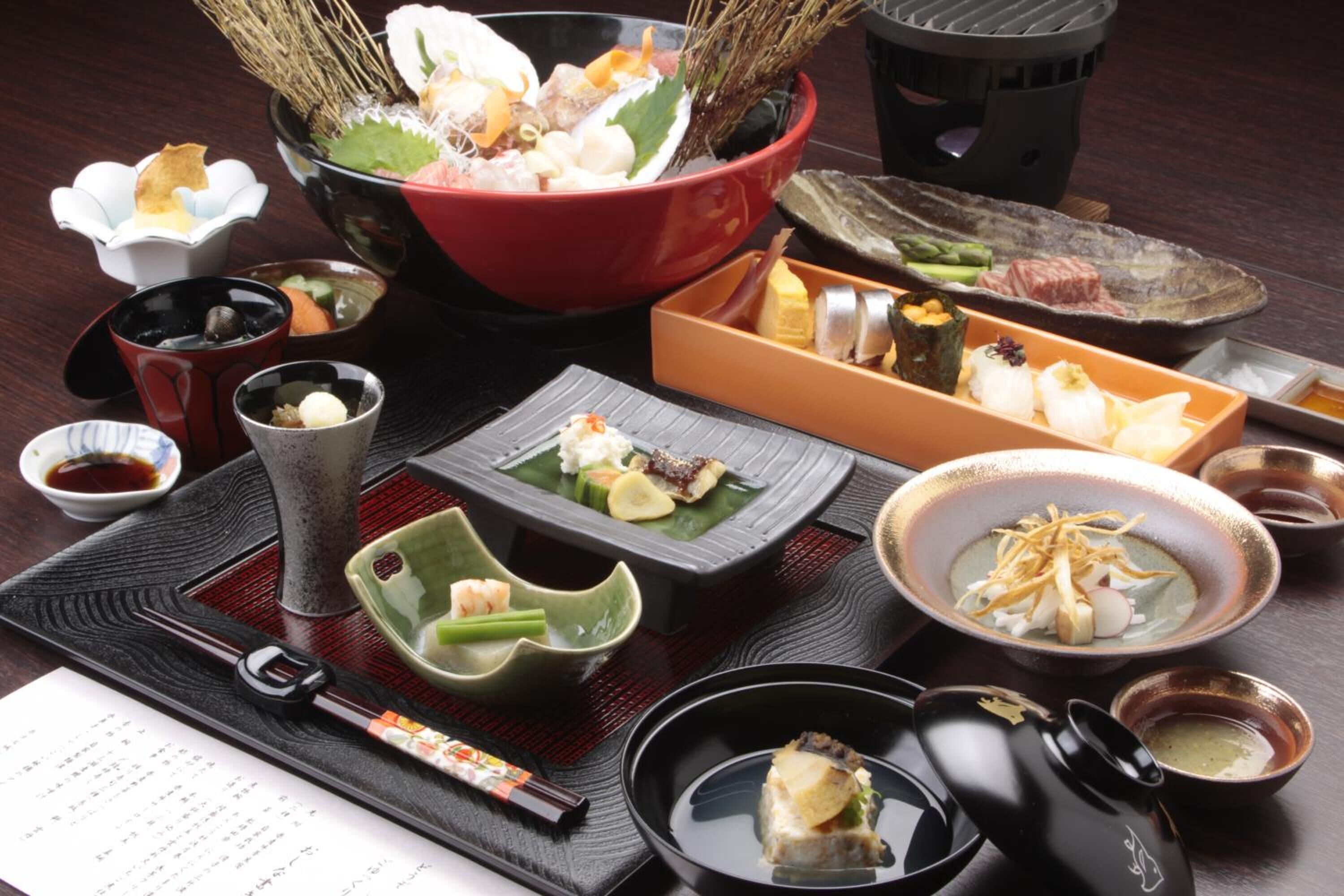A variety of Japanese dishes arranged on a table, including sushi, sashimi, and other delicacies, accompanied by small bowls of sauces and condiments.