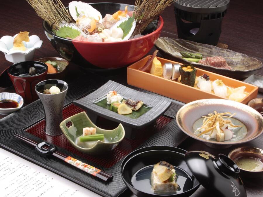 A variety of Japanese dishes arranged on a table, including sushi, sashimi, and other delicacies, accompanied by small bowls of sauces and condiments.