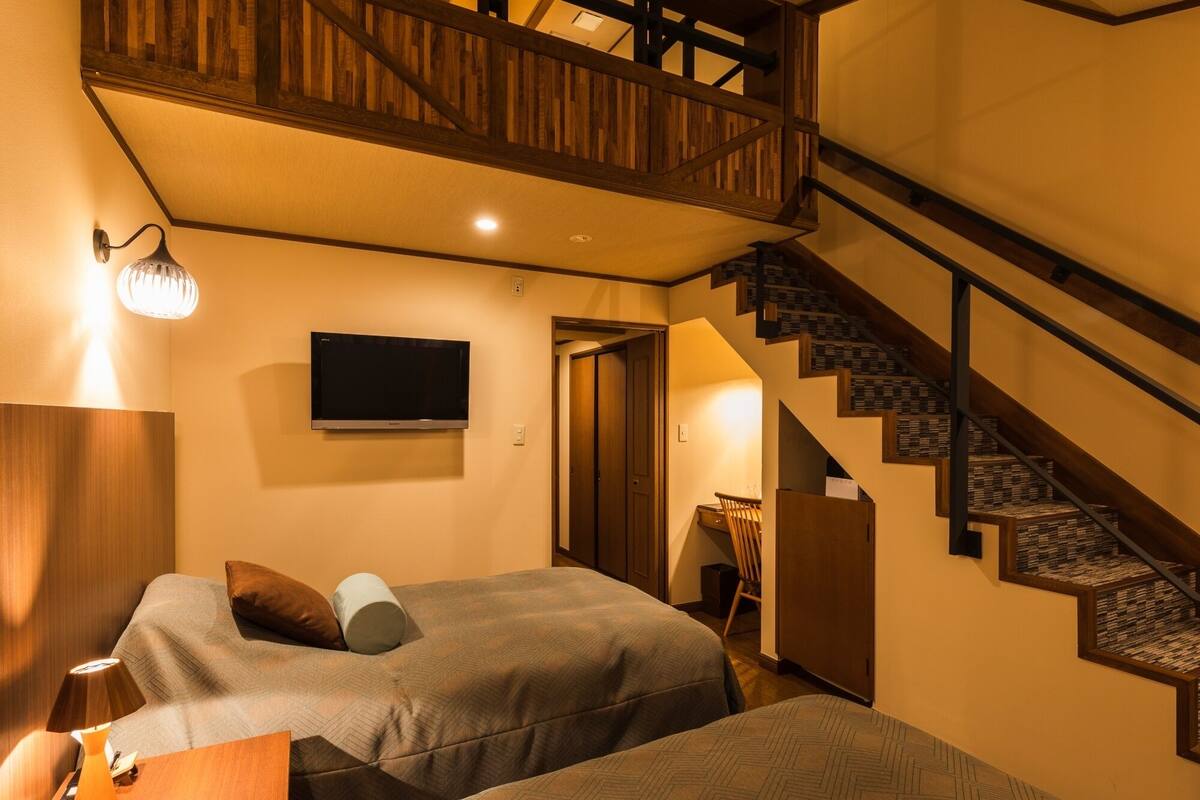 Ein Schlafzimmer mit zwei Betten, einem Fernseher, einer Treppe und einer Holzbalkendecke.