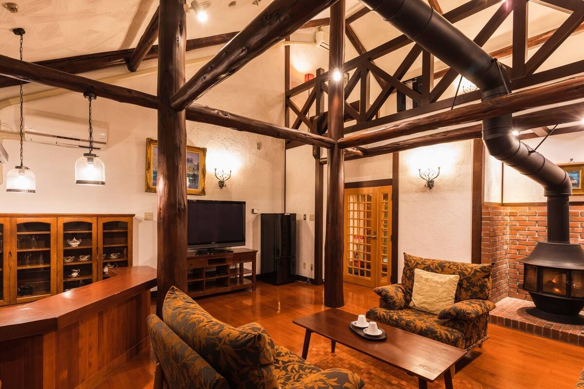 Ein gemütliches Wohnzimmer mit Holzbalken, Kamin, Fernseher und einer Bar.