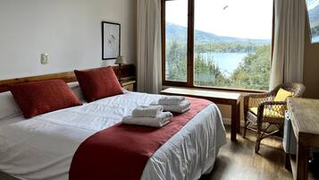 Habitación de hotel con una cama grande, una silla, una mesa y una ventana con vistas panorámicas.