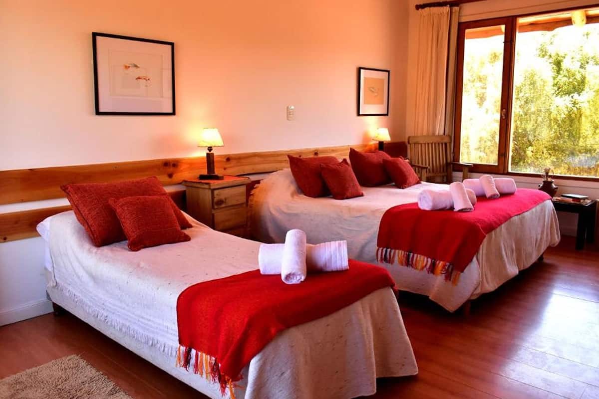 Ein Hotelzimmer mit zwei Betten, jeweils mit roter Decke und Kissen, einem Holzkopfschild, Nachttischlampen und gerahmten Bildern an den Wänden.