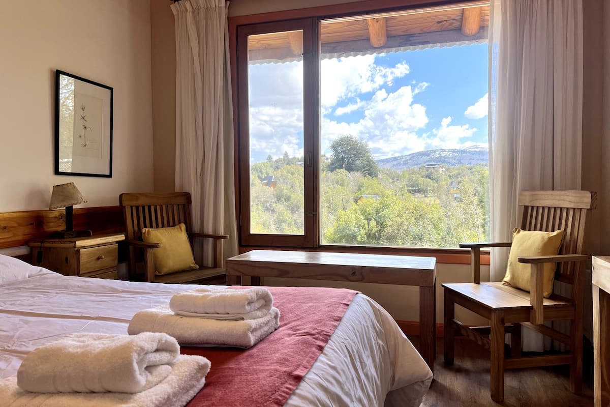 Ein Hotelzimmer mit zwei Betten, einem Holztisch, Stühlen und einem großen Fenster mit schöner Aussicht.