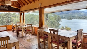 Un espace repas en bois doté de grandes fenêtres donnant sur un lac et des montagnes.