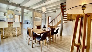 Un comedor amplio con una mesa y sillas de madera, un muro decorativo de piedra y una escalera que conduce a un nivel superior.