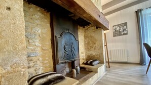 Una chimenea de piedra con una placa decorativa, un banco de madera y un radiador en una habitación con suelo de madera y pared blanca.