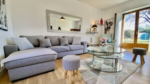 Una sala moderna con un sofá seccional gris, una mesa de centro de vidrio y un reposapiés redondo.