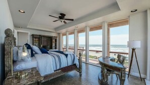 Una camera da letto con un letto grande, un ventilatore a soffitto, un comodino, un tavolo con sedie e vista sull'oceano.