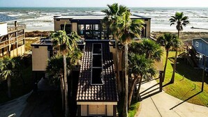 Una moderna casa a due piani con tetto in tegole, circondata da palme e con vista su una spiaggia.