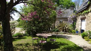Un bâtiment en pierre avec une allée gravillonnée et un jardin comprenant une table ronde et des chaises.