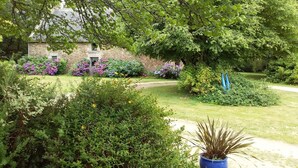 Un bâtiment en pierre avec un jardin à l’avant, entouré d’une végétation luxuriante et de plantes en fleurs.