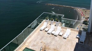 A rooftop pool with clear water, surrounded by lounge chairs and potted plants, overlooking a beach and ocean. - Apartamentos  Cartagena 01 (Cartagena)