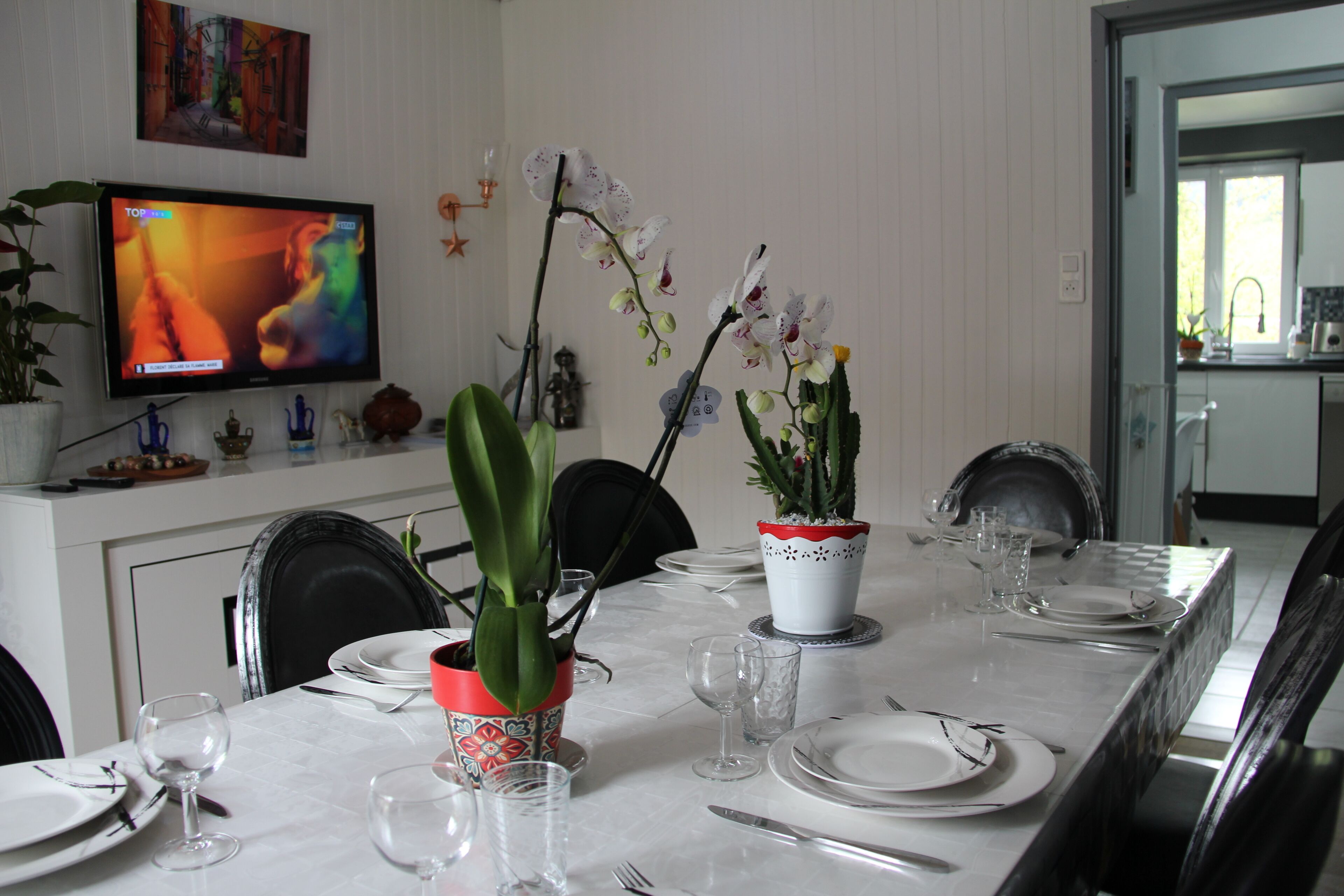Een eethoek met een televisie, potplanten en een net gedekte tafel.