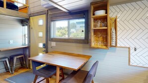 Une cuisine de taille réduite avec une table en bois et deux chaises, une fenêtre offrant une vue agréable et un mur orné d’un motif en chevrons.