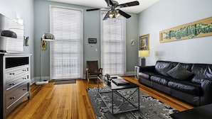 A living room with a black leather sofa, a coffee table, a floor lamp, and a ceiling fan.