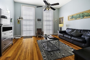 A living room with a black leather sofa, a coffee table, a floor lamp, and a ceiling fan.