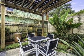 An outdoor patio with a wooden pergola, a table with chairs, and various plants.