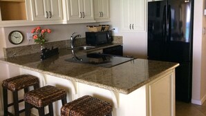A kitchen with white cabinets, a black refrigerator, a microwave, a sink, and three woven stools. - Best Kept Secret on Oahu ! (Waiʻanae)