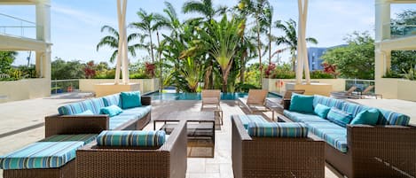 A covered outdoor seating area with wicker furniture and a pool in the background.
