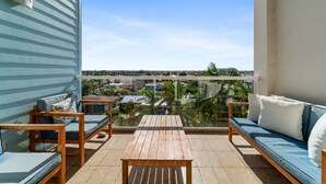 Un balcón con una mesa de madera y dos sofás, con vista a una zona residencial con casas y palmeras.