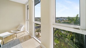 Un balcón con vistas a un paisaje urbano, una silla blanca y una mesa pequeña.