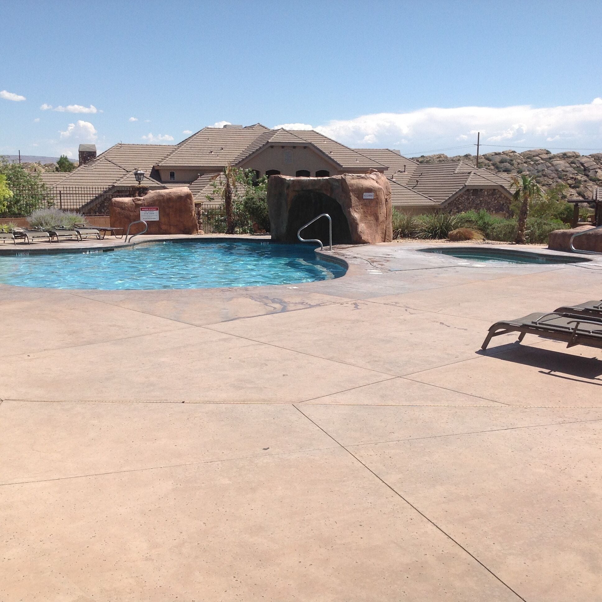 A pool area with a hot tub, lounge chairs, and a rock formation.