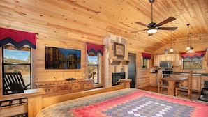 Un interior de cabaña acogedor con una cama grande, una chimenea, un comedor y una cocina.