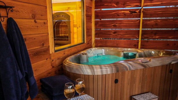 Una cabaña de madera con un jacuzzi, una mesa con dos copas de vino y una toalla colgada en la pared.