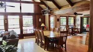 A spacious dining area with a wooden table and chairs, large windows, and a ceiling fan. - Windy Break Lake Front House (Gouldsboro)