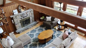 A cozy living room with a stone fireplace, wooden beams, a sofa, and a coffee table. - Windy Break Lake Front House (Gouldsboro)