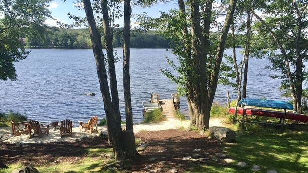 A lakeside campsite with wooden chairs, a canoe, and a dock leading to the water. - Windy Break Lake Front House (Gouldsboro)